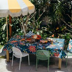 an outdoor table set up with food and umbrellas in the background, surrounded by greenery