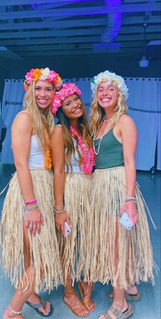 three young women in hula skirts posing for the camera with flowers on their heads