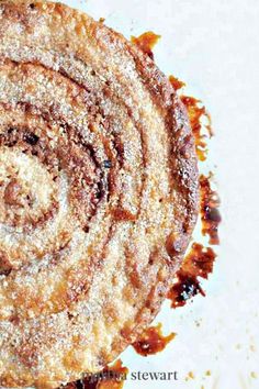 a cinnamon roll on a white plate covered in powdered sugar and brown syrups