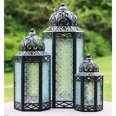 three lanterns sitting on top of a table next to each other in front of trees