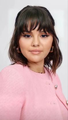 a close up of a person wearing a pink shirt and earrings with bangs on her head