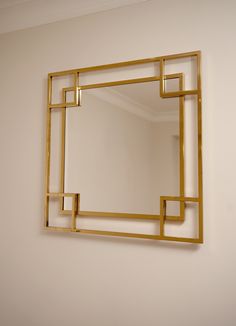 a mirror that is on the wall in front of a white wall with a gold frame