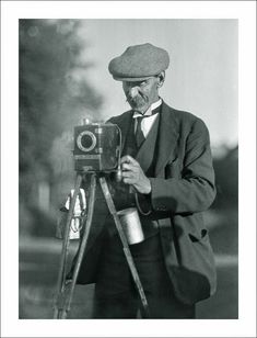 black and white photograph of a man holding a camera with a tripod in front of him