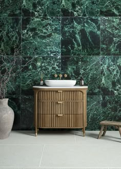 a bathroom with green marble walls and flooring next to a white sink on top of a wooden cabinet