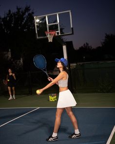 a woman holding a tennis racquet on top of a tennis court at night