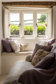 a window seat with pillows on it in front of a white wall and two windows