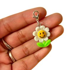 a hand holding a keychain with a smiley face and flower on the front