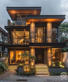 a modern house with stairs leading up to the second floor and lights on it's windows