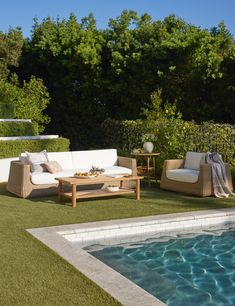 an outdoor living area next to a swimming pool with grass and furniture on the lawn