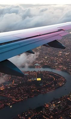 the wing of an airplane flying over a city at night with clouds in the sky