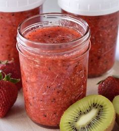 kiwis and strawberries sit on a cutting board next to jars of fruit