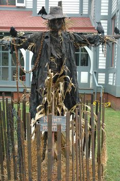 a scarecrow statue in front of a house with crows perched on it's head