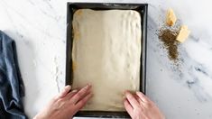 two hands reaching into a baking pan filled with dough