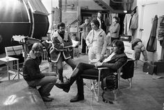 black and white photograph of people sitting in chairs around an engine room with two men standing next to them