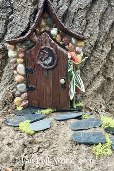 a small wooden house sitting next to a tree with rocks and leaves on the ground