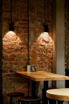 two wooden tables sitting next to each other in front of a brick wall with lights on it