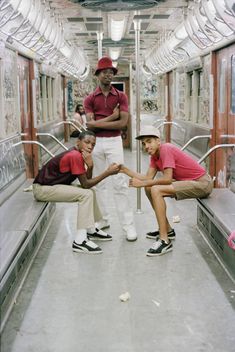 three men in red shirts and white pants are on a subway train with their hands together