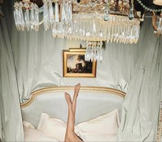 a woman laying in bed under a chandelier with her feet on the pillow