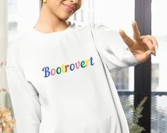 a woman wearing a white sweatshirt with the word bootrovet written in multicolored letters