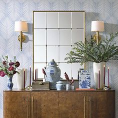 a table with vases and flowers on it in front of a large mirror over a dresser