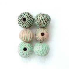 four ceramic balls are sitting on a white surface, one is pink and the other has green speckles