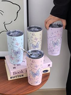 three different colored tumblers with butterfly designs on them, one is holding a straw