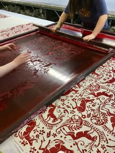 two people working on an intricately designed piece of art with red and white fabric