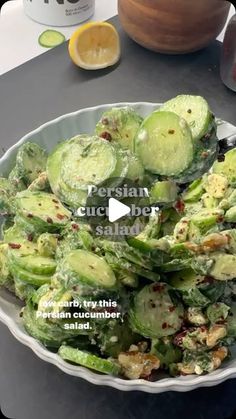 a white bowl filled with cucumber salad on top of a table next to an orange slice