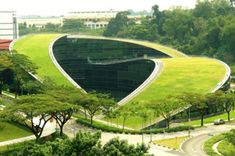 an unusual building in the middle of a green park with trees and grass on both sides