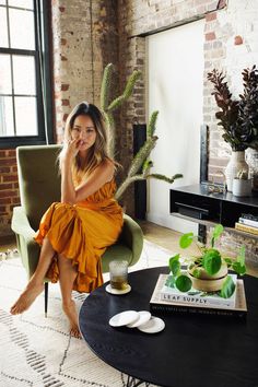 a woman sitting in a chair next to a table with a plant on top of it