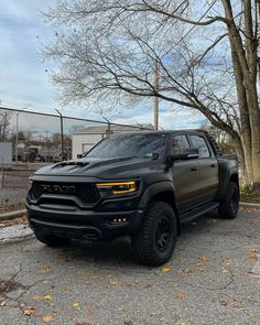 a black truck is parked in the parking lot next to some trees with no leaves on them