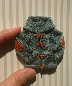 a hand holding a small knitted sweater with orange stars on the front and bottom