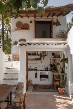 an outdoor kitchen with pots and pans hanging from the ceiling, next to a wooden table