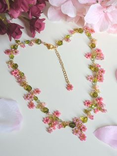 a necklace with pink flowers and green beads is on the table next to some petals