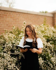 a woman standing in front of flowers reading a book