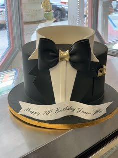 a black and white cake with a bow tie on it's top is sitting on a table