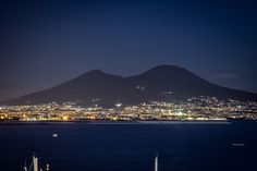 the city lights are lit up in the night sky over the ocean and mountain range