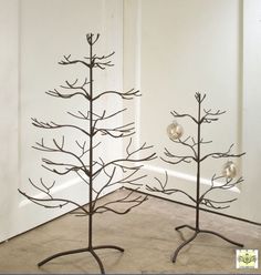 two metal tree sculptures sitting on top of a floor next to each other in front of a white wall