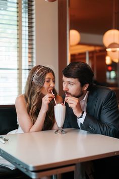 a man and woman sitting at a table drinking milkshakes