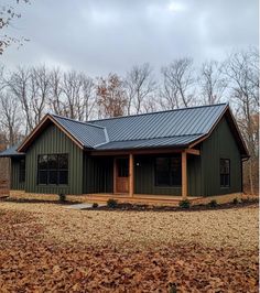 a green house with a metal roof surrounded by trees and brown leaves on the ground