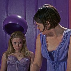 two women standing next to each other in front of a purple wall