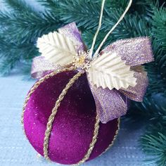 a purple ornament hanging from a christmas tree with a bow on it's side