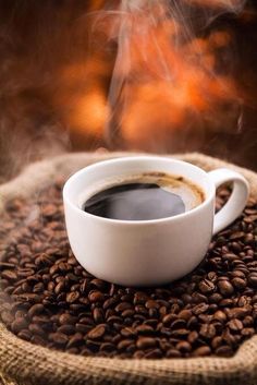 a cup of coffee sitting on top of a pile of coffee beans next to a fire