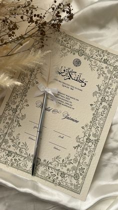 an ornate wedding card with a feather quill resting on it's cover next to some dried flowers