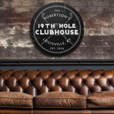 a brown leather couch in front of a brick wall with a sign that reads 19th hole clubhouse