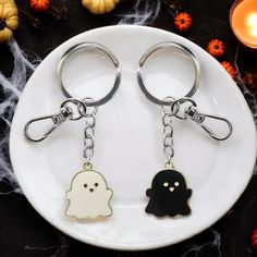 two keychains with ghost faces on them sitting on a plate next to candles and pumpkins