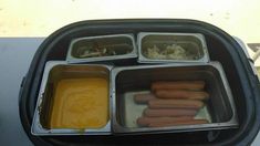 four trays with hot dogs, mustard and condiments in them sitting on a table