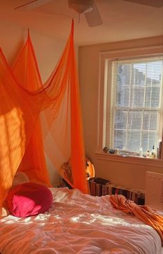 a bed with orange netting hanging from it's sides and pillows on the bottom