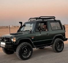 a black suv with two people in the driver's seat driving down a desert road