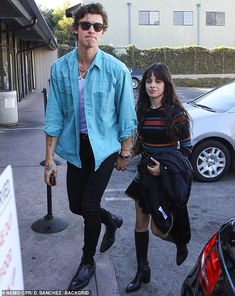 a man and woman walking down the street holding hands with one another, both wearing black boots